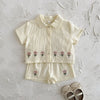 A cream baby cotton shirt and shorts set with a small pink flower pattern.