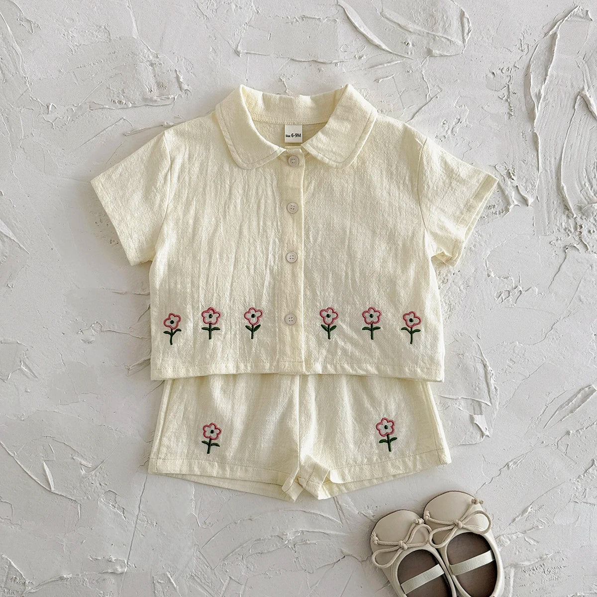 A cream baby cotton shirt and shorts set with a small pink flower pattern.