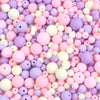 A close-up view of numerous matte acrylic beads in various shades of pink, purple, and white.