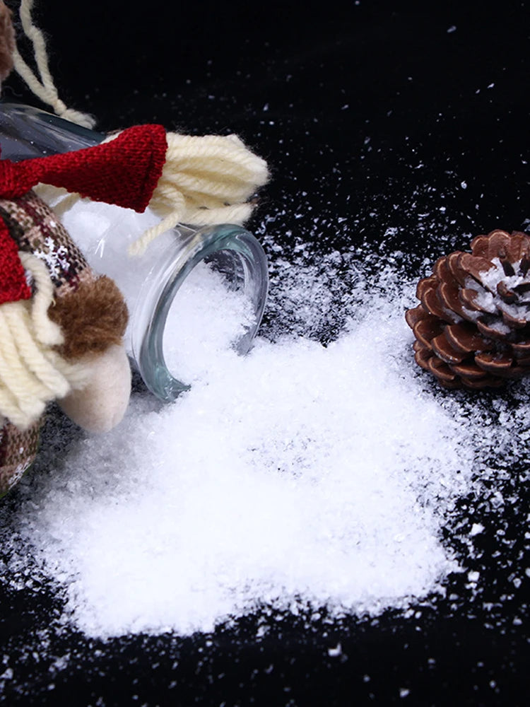 A glass jar filled with white artificial snow powder next to a knitted reindeer decoration on a black background.