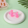 A bright pink translucent stress ball squishy toy resting on a white plate with a pink background.