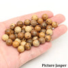 A hand holds a collection of natural stone round beads for jewelry making in various earthy tones.
