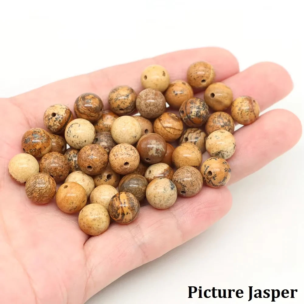 A hand holds a collection of natural stone round beads for jewelry making in various earthy tones.
