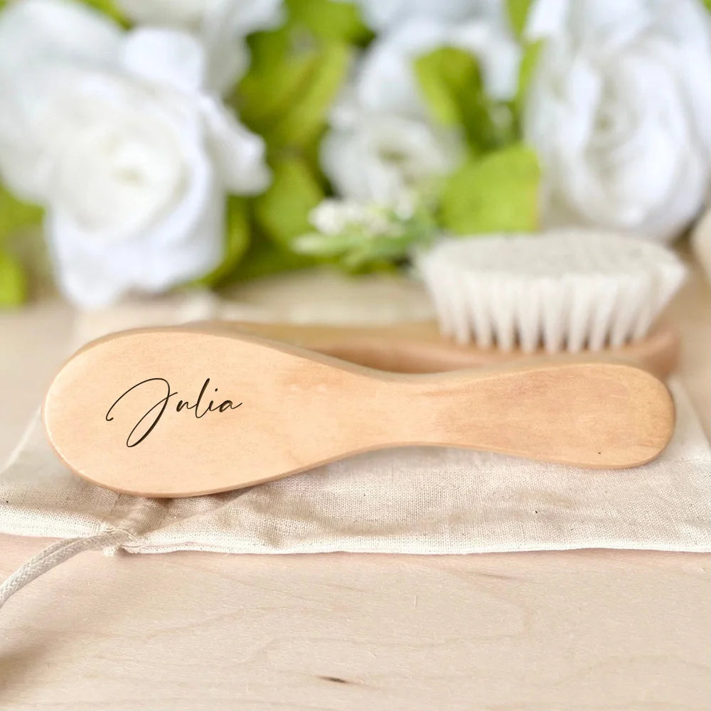 A light wooden baby brush and comb set with an engraved name lying on a beige cloth.