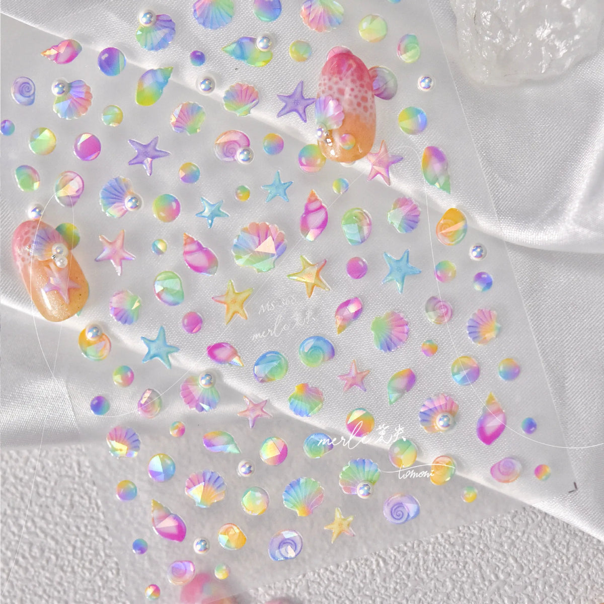 Glittery stickers featuring gold shells and starfish in various pastel colors scattered on white fabric.