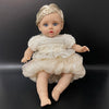 A lifelike 14-inch reborn baby doll with blue eyes and a white ruffled outfit.