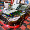 A black Ford Fusion sedan with a holographic chrome vinyl wrap finish parked on a red and black checkered floor.