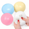A hand holds a white jumbo slow-rising cheese squishy stress relief toy next to three colored balloons: blue, yellow, and pin