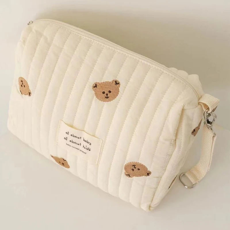 A cream quilted baby diaper caddy organizer with small bear-themed patches and attached stroller straps.