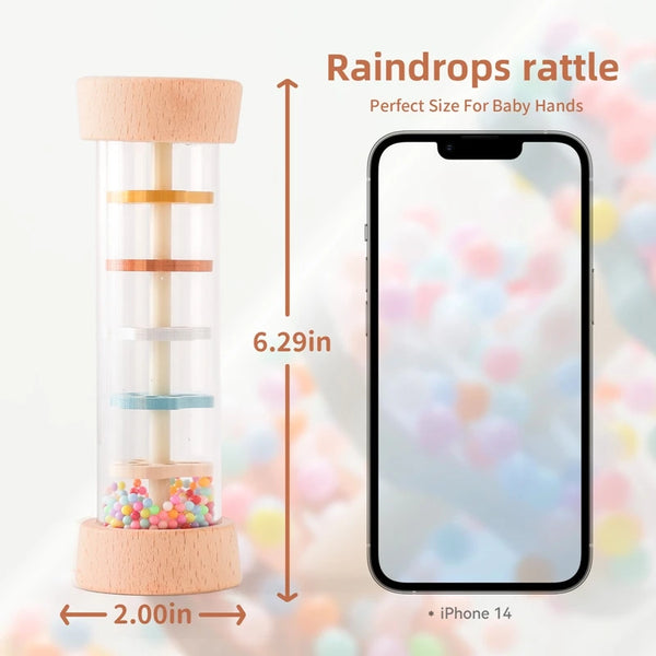 Un hochet de pluie en bois avec des anneaux colorés et une base rose, à côté d'un iPhone 14 pour l'échelle.