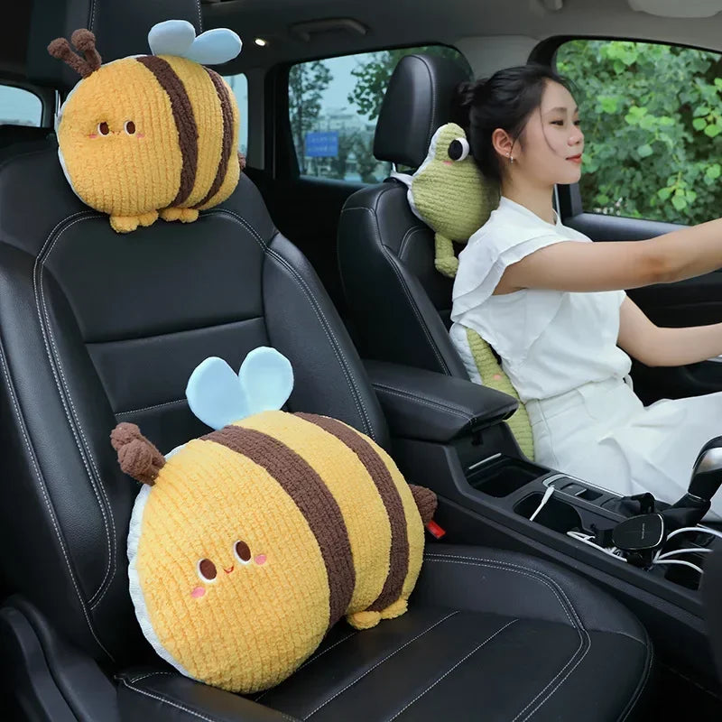 Two yellow plush bee lumbar support pillows with brown stripes and a green plush animal sitting in the back seat of a car.