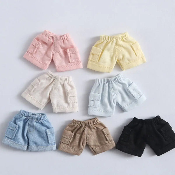 A collection of mini jeans shorts in pink, yellow, beige, and blue are displayed on a white background.