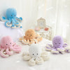 A collection of adorable plush octopus toys in various colors including blue, orange, pink, and purple resting on a white sur