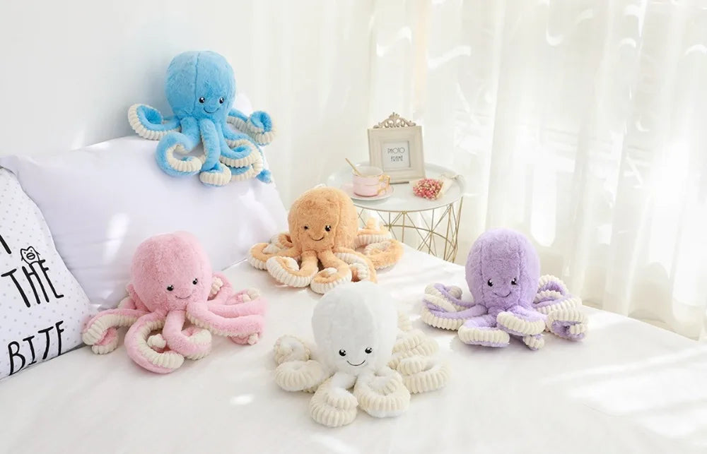 A collection of adorable plush octopus toys in various colors including blue, orange, pink, and purple resting on a white sur