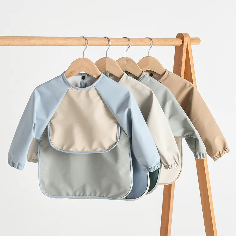 A display of light blue and beige waterproof long-sleeved baby bibs hanging on a wooden rack.