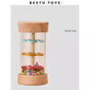 A clear glass jar filled with colorful beads and a wooden top, used as a rain sound shaker toy.
