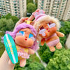 A hand holds a Crybaby Vacation Mode On vinyl figure blind box with pink hair and light purple clothing.