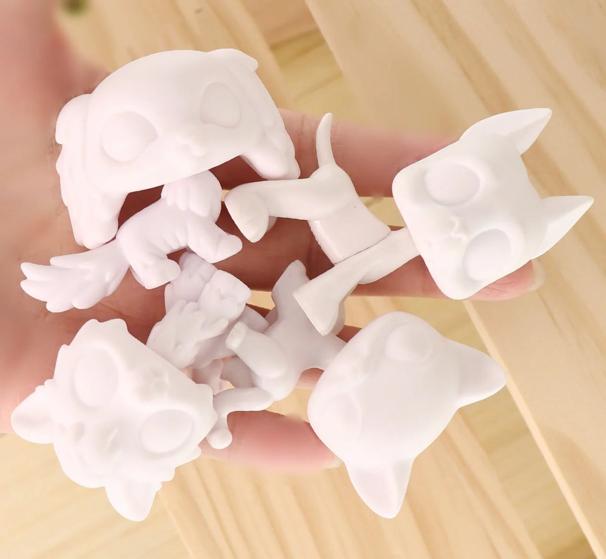 A hand holds several white, customizable bobble head pet figures for a DIY kit.