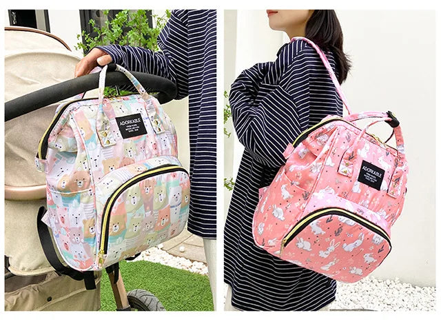 A pink cartoon print waterproof diaper bag being held by a woman in a striped shirt.