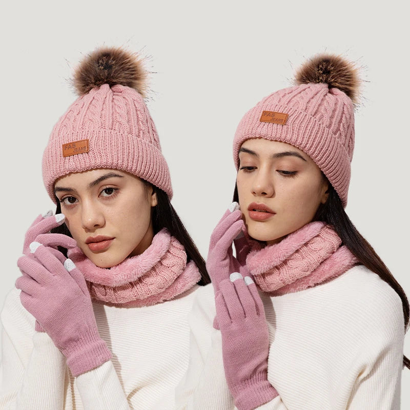 A woman models a pink knit winter hat, scarf, and gloves set with faux fur pom on a light background.