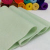 A stack of light green felt fabric sheets next to various colored yarn spools.