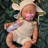 A hand-painted silicone reborn doll with pink ears and a light pink knitted outfit lying on green fabric.