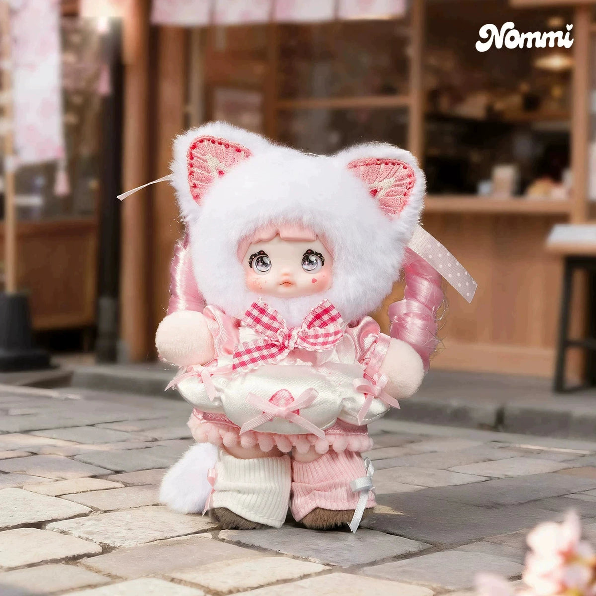 A fluffy white cat plush keychain with pink accents and a bow, displayed on a stone surface.