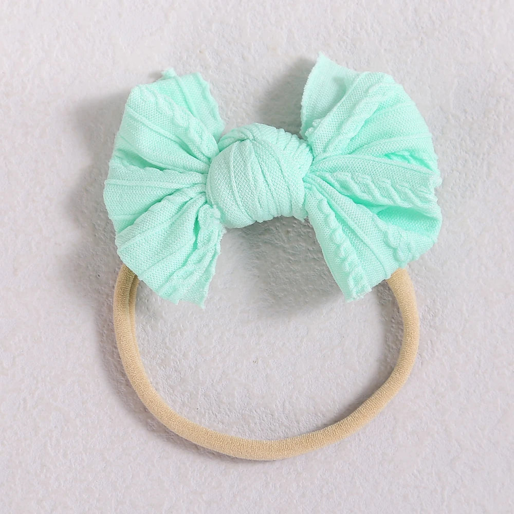 A light mint green fabric bow headband with a beige elastic band lying on a white surface.