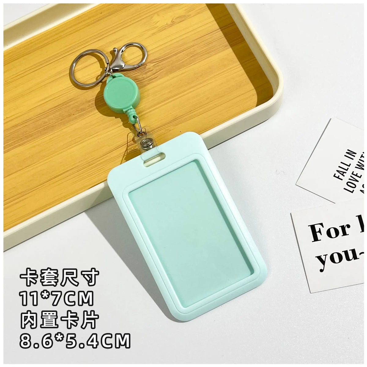 A light mint green retractable ID badge holder with a clip and keychain is displayed on a wooden tray.