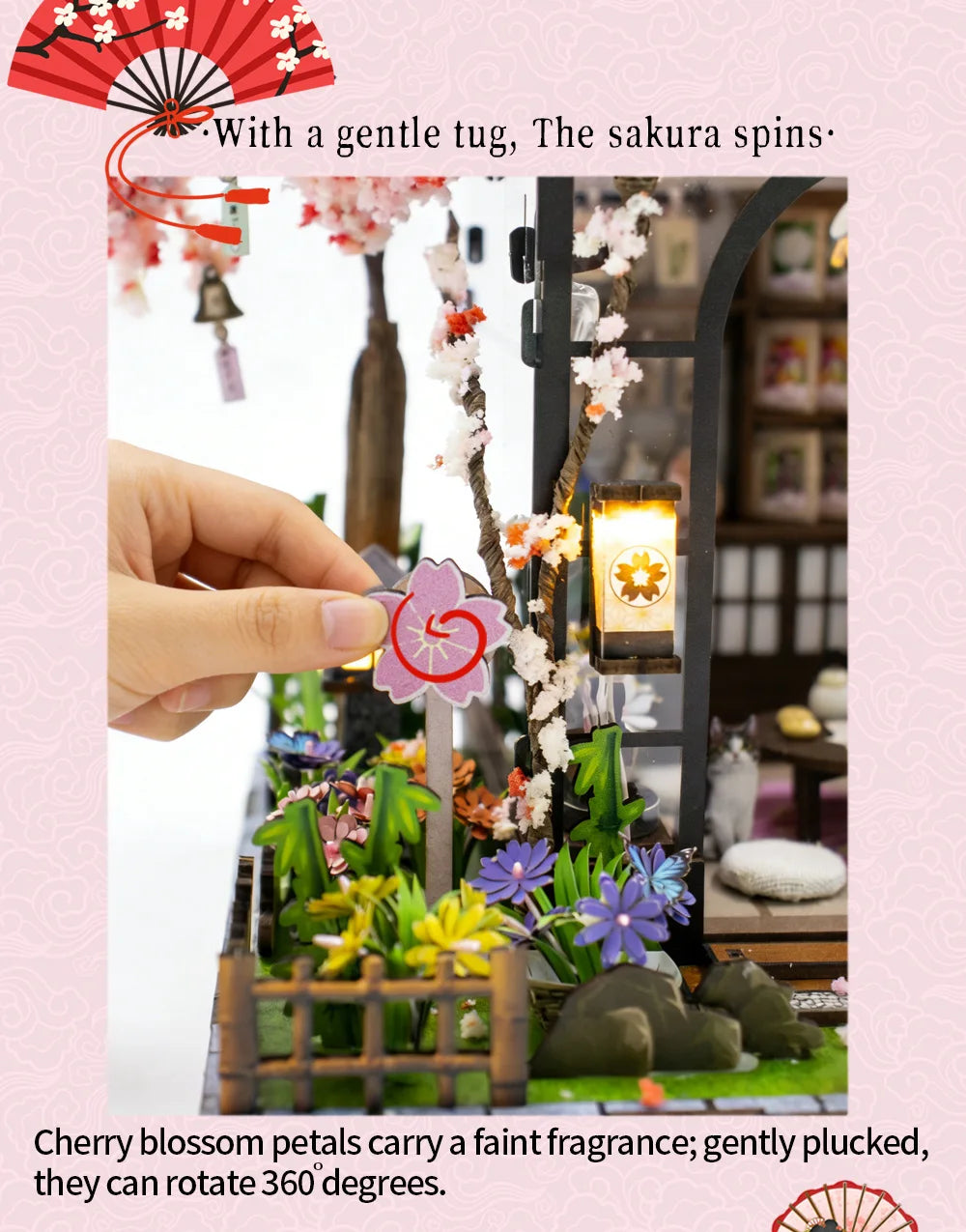 A hand gently plucks cherry blossom petals from a branch inside a miniature Japanese tea house display.
