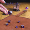 A hand places a purple die onto a brown leather tray with other dice and a storage bag visible in the background.