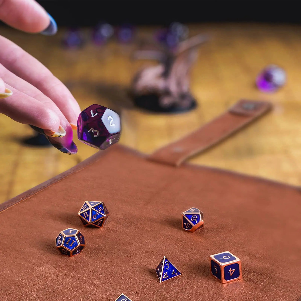 A hand places a purple die onto a brown leather tray with other dice and a storage bag visible in the background.