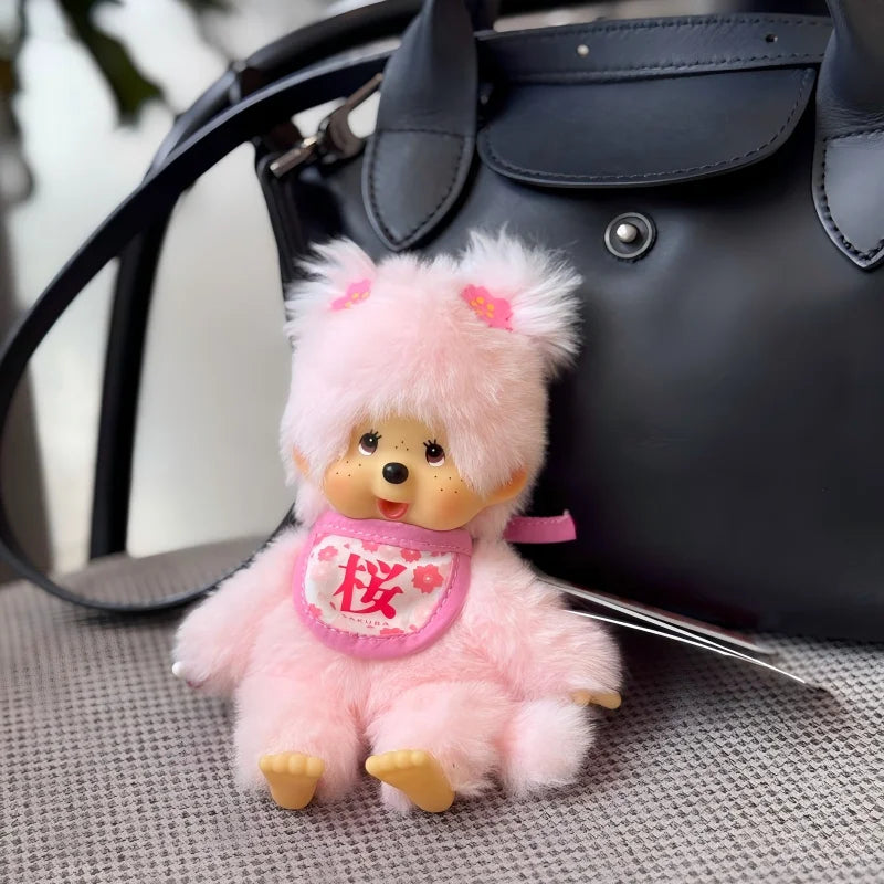 A fluffy pink cartoon bear plush toy resting on a gray surface next to a black handbag.