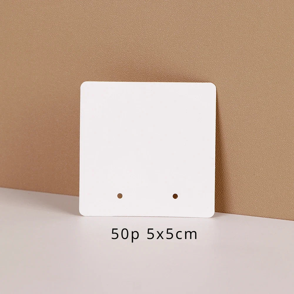 A white square jewelry display card with two holes is shown against a beige background.