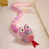 A pink and purple patterned plush snake toy with large eyes and a red tail resting on a white surface.