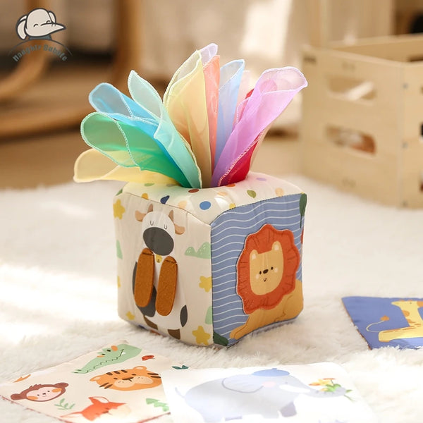 Montessori-Sensorbox für Babys mit Tiergesichtern und buntem Papiertuch auf einem weißen Fluffersaum