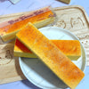 A rectangular orange butter stick squishy toy is displayed on a white plate next to its packaging.
