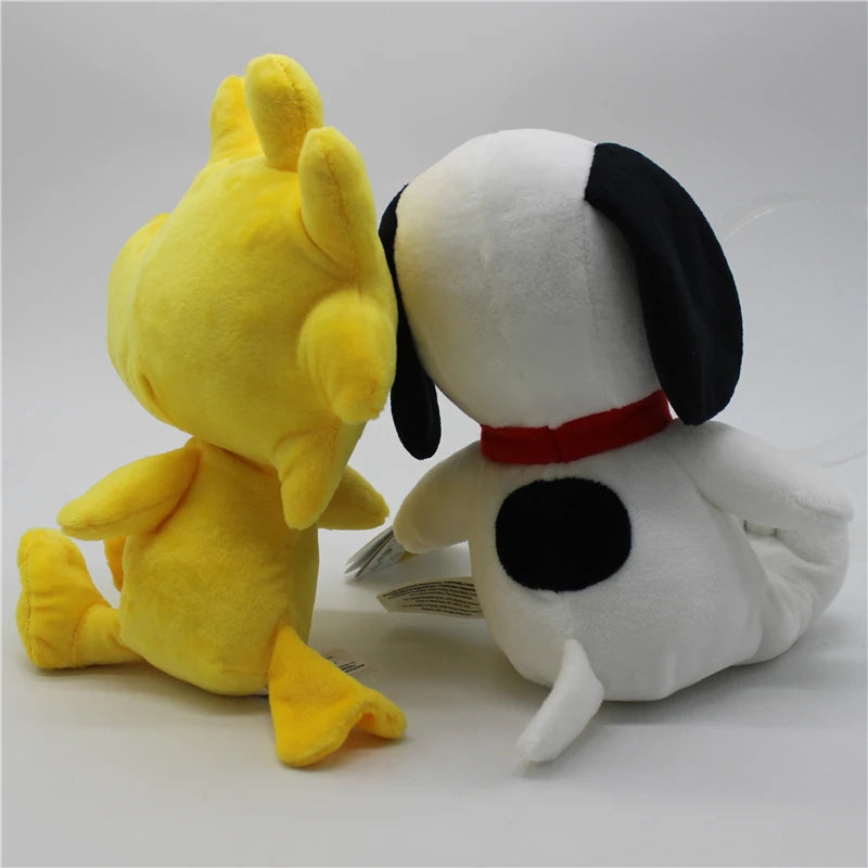 A yellow Snoopy plush toy next to a white Woodstock plush toy.