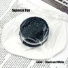 A black and white silicone biscuit squishy stress relief toy resting on a white plate.