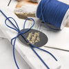 A roll of blue braided ribbon used for crafting and gift wrapping, tied with a black tag.