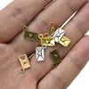 A hand holds a collection of vintage envelope charms in gold and silver tones for jewelry making.