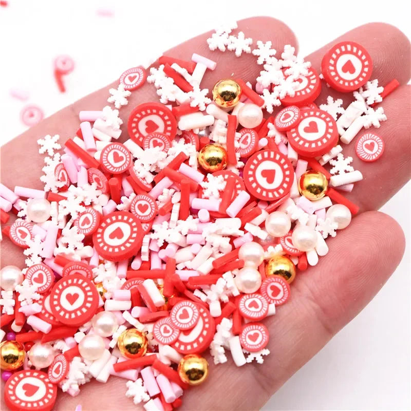 A hand holds a pile of red and white polymer clay slices, including heart shapes and various decorative elements for DIY craf