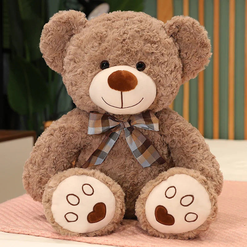 A brown teddy bear plush pillow with a plaid bow resting on a pink surface.