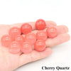A hand holds several polished, spherical pieces of cherry quartz crystals.