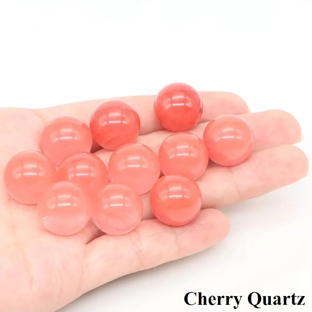 A hand holds several polished, spherical pieces of cherry quartz crystals.