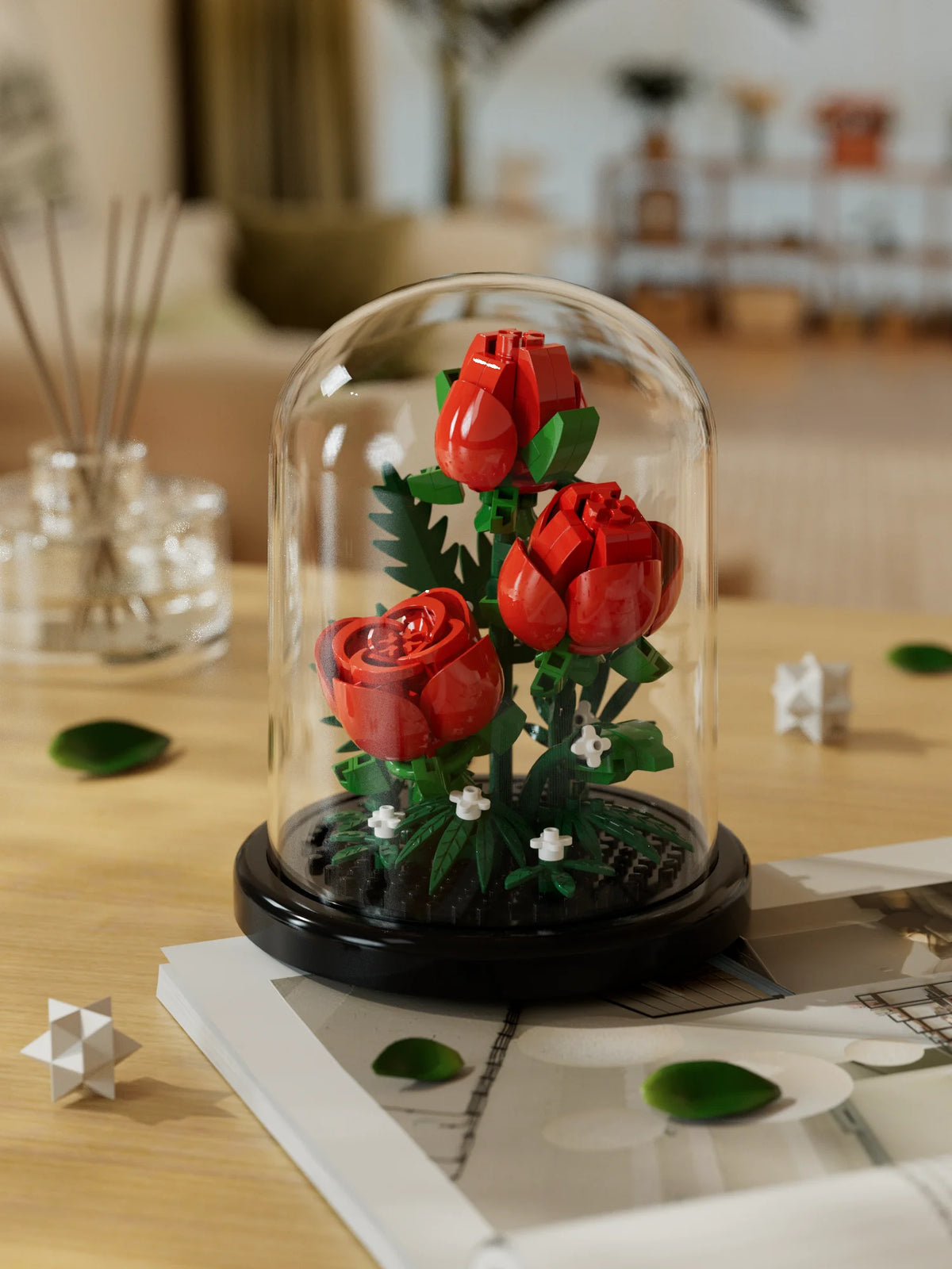 A glass dome display of a buildable eternal rose flower kit featuring vibrant red roses and green foliage.