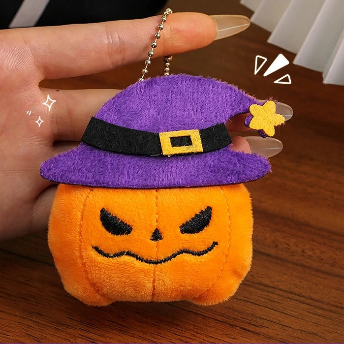 A hand holds a Halloween plush keychain set featuring a purple witch hat, an orange pumpkin body, and yellow bat charms.