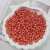 A pile of pink oval glass rice grain beads for jewelry making in a white dish.
