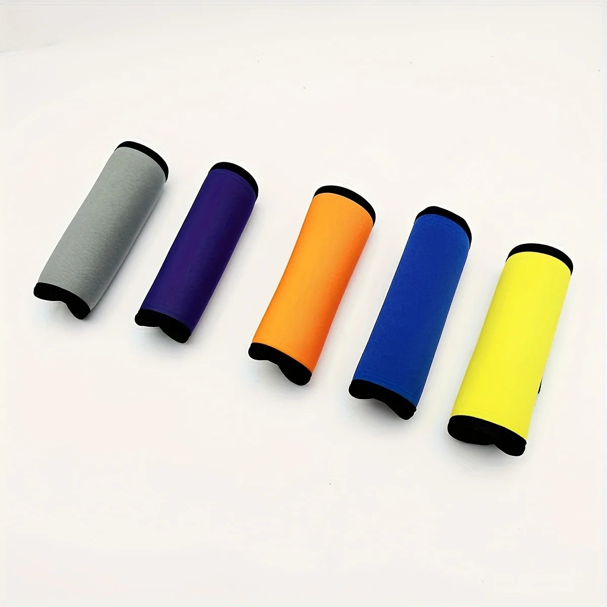 Five colored neoprene luggage handle covers in gray, purple, orange, blue, and yellow laid out on a white surface.