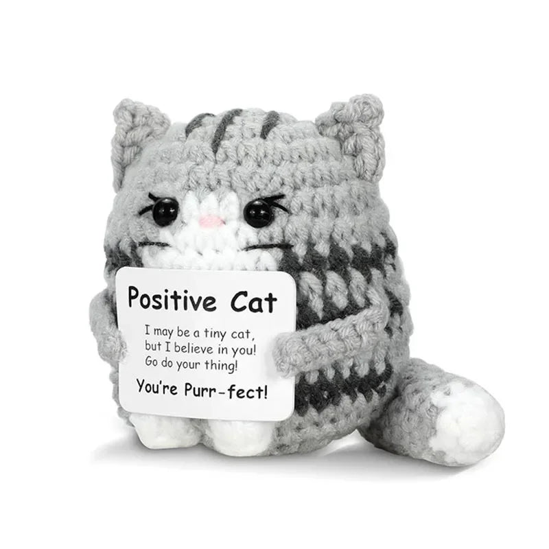 A handmade gray and white crochet cat figurine with a sign that reads You're Purr-fect